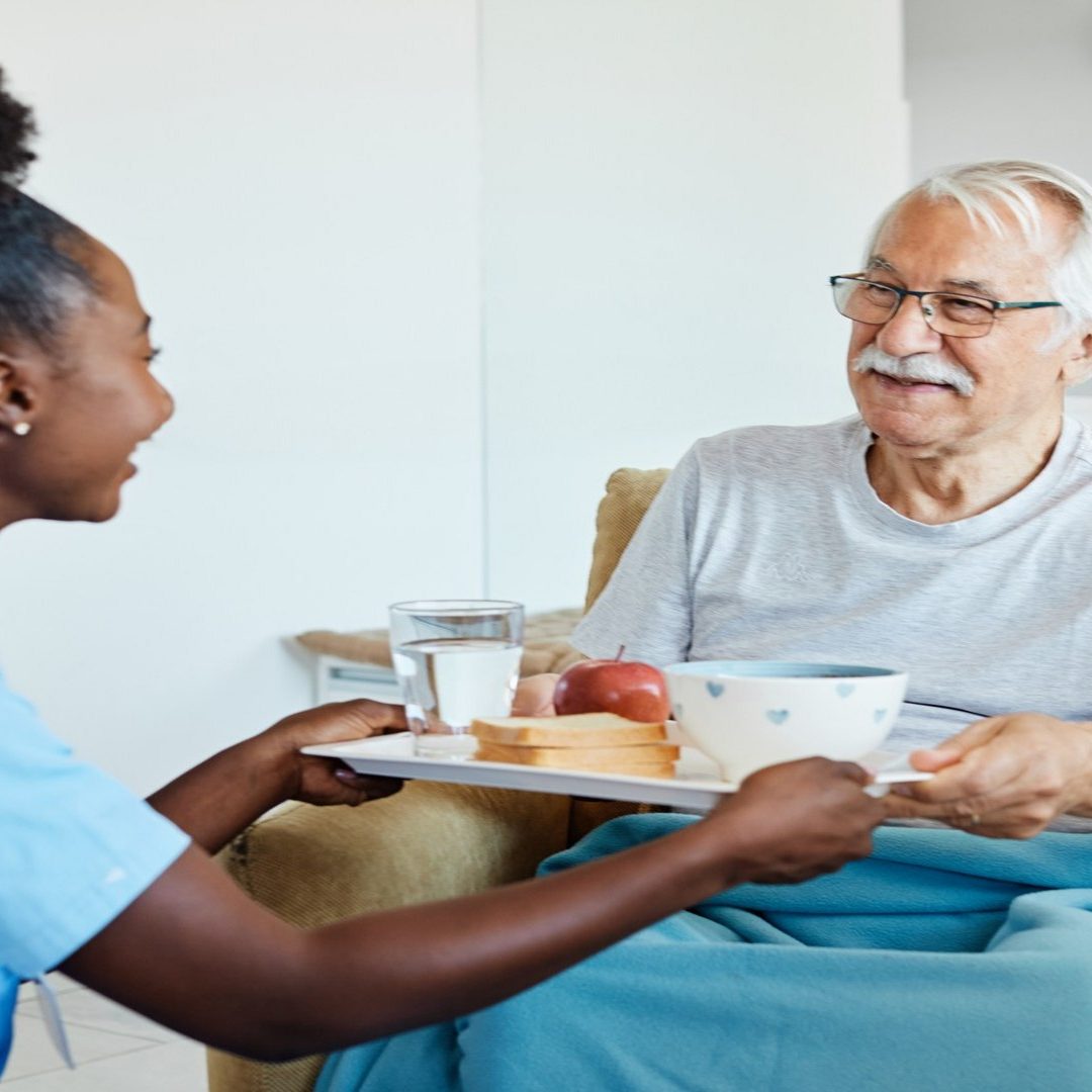 Caregiver Serving A Meal To Senior Man